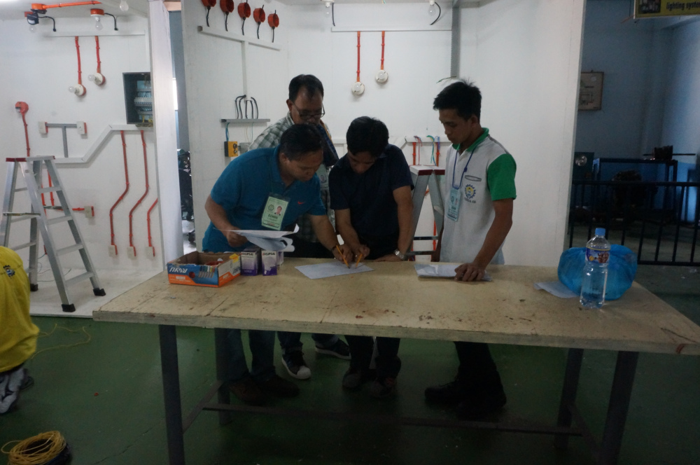 Tinitingnan ng mga lalaki ang isang disenyo para sa electrical installation sa isang training session tungkol sa Electrical Installation and Maintenance (EIM). Ang EIM ay isang technical course ng TESDA hinggil sa electrical and lighting wiring and maintenance para sa residential buildings na gumagamit ng boltahe na hindi lalagpas sa 600 volts (TESDA-Mimaropa)